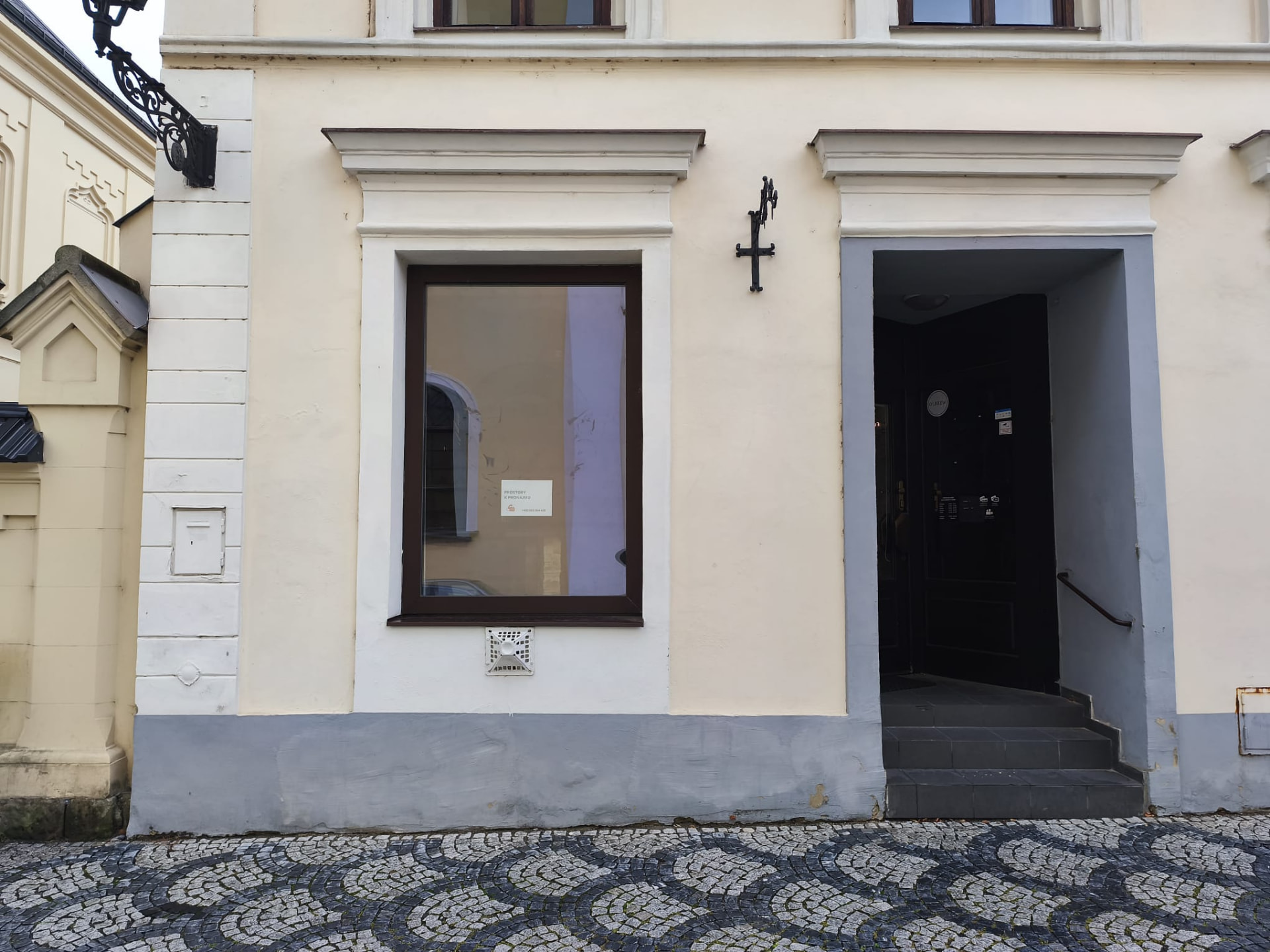 Prázdná výloha v ulici u náměstí s cedulí Prostory k pronájmu