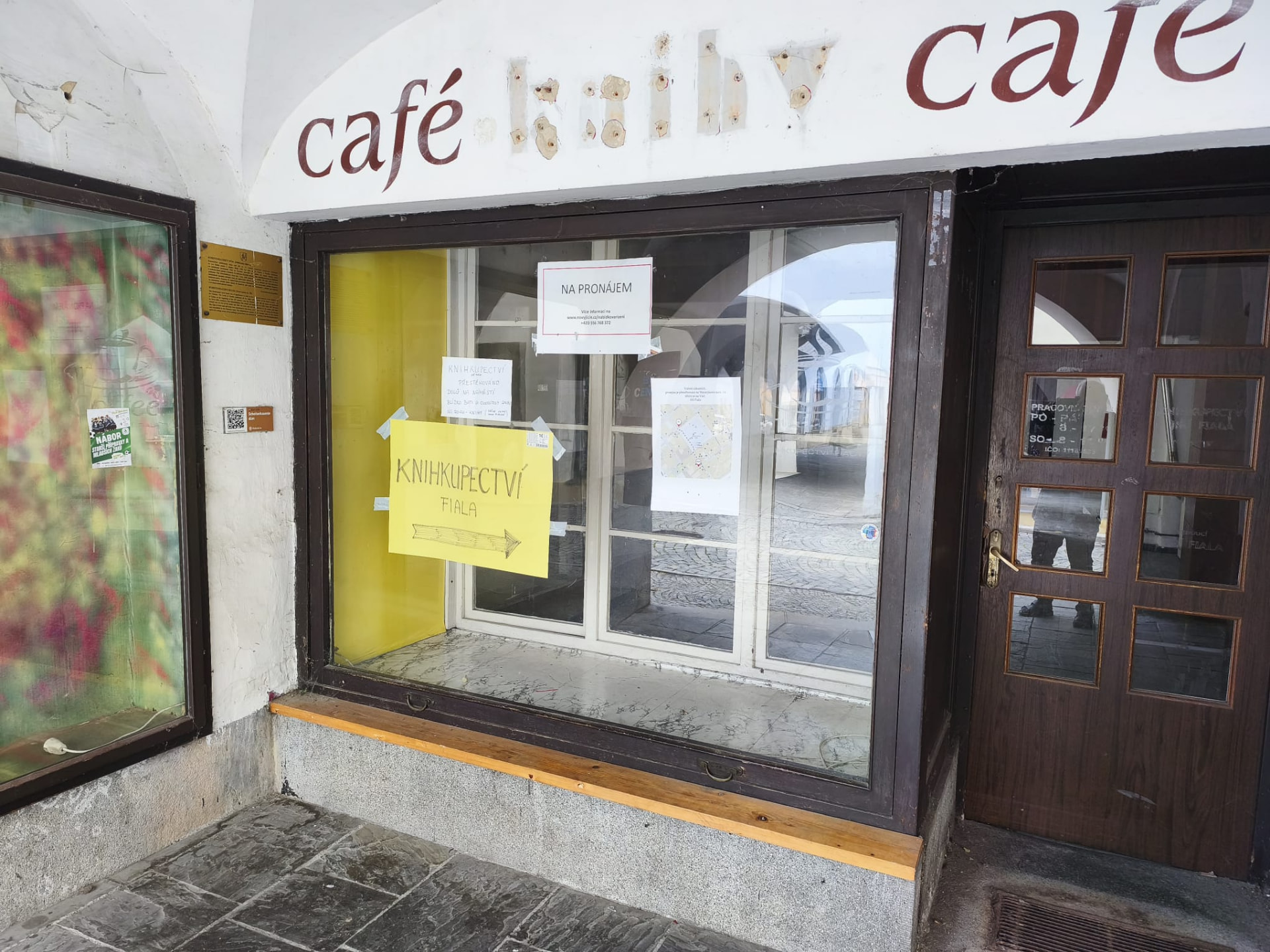 Bývalá kavárna a knihkupectví na náměstí s cedulí Na pronájem